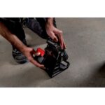 Projecteur LED sans fil noir et rouge avec poignée, posé au sol sur chantier