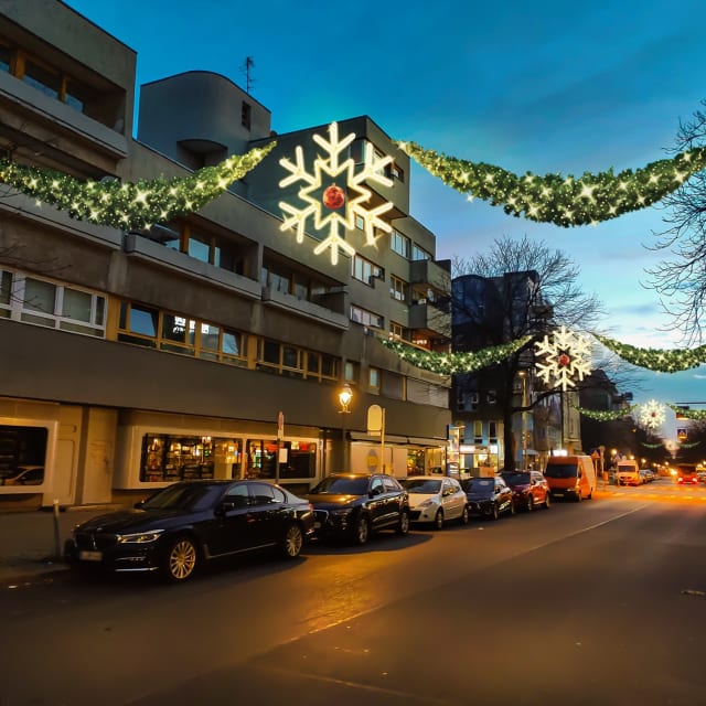 Rue au crépuscule avec flocons lumineux et guirlandes suspendus entre les bâtiments