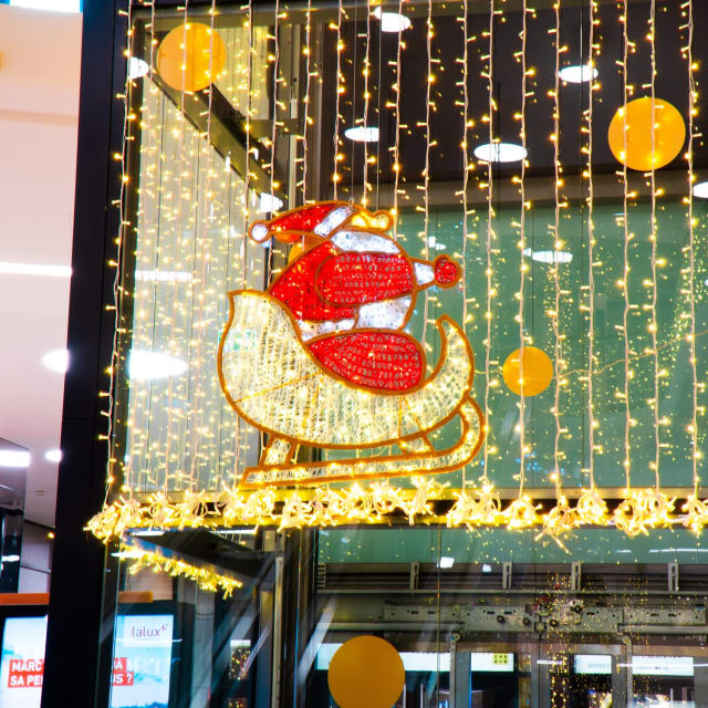 Père Noël rouge et blanc dans un traîneau doré, suspendu devant des rideaux lumineux