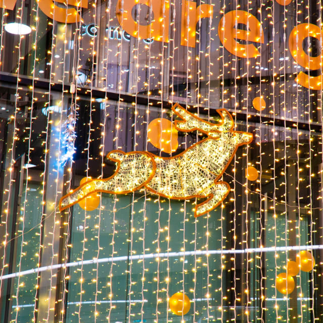 Renne doré lumineux en plein bond devant un rideau de LED et une vitrine décorée