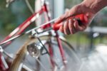 Main utilisant un tournevis rouge et noir sur un élément métallique près de la roue d’un vélo